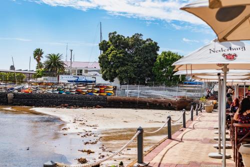 a beach with an umbrella and people sitting on the beach at The Willets Boutique Hotel in Simon's Town in Simonʼs Town