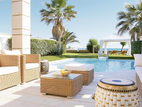a patio with wicker furniture next to a swimming pool at Grecotel Creta Palace in Rethymno Town