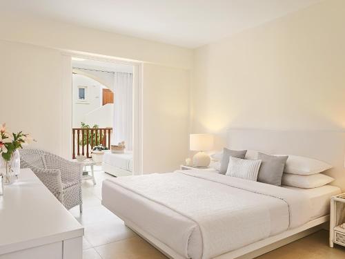 a white bedroom with a large bed and a table at Grecotel Marine Palace & Aqua Park in Panormos Rethymno