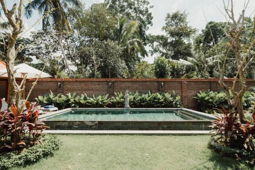 a swimming pool in a garden with a brick wall at Maha Villa Kelating in Krambitan