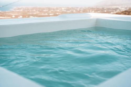 a bath tub filled with blue water with a view at Leon Luxury Suites in Imerovigli