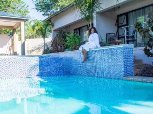 a woman sitting on a wall next to a swimming pool at The Telescope Boutique Lodge in Victoria Falls