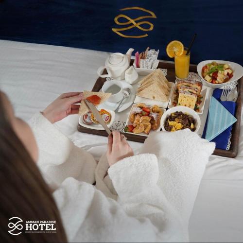 a person sitting in bed with a tray of food at Amman Paradise Hotel in Amman