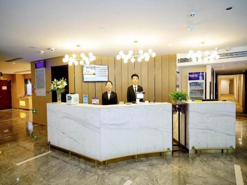 two men standing at a counter in a lobby at Metropolo Hotel Qingdao Wusi Square Xiaomaidao in Qingdao