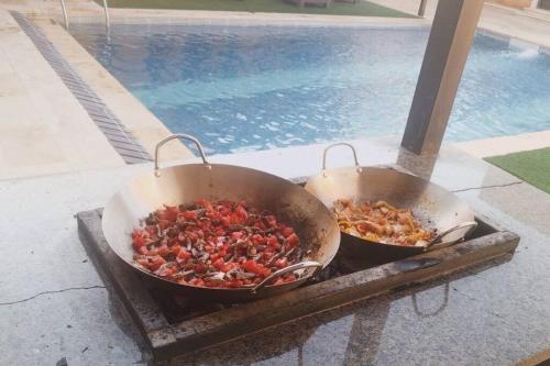 two large pans of food on a table next to a pool at Private Pool - Relax Chalet Deadsea in Amman
