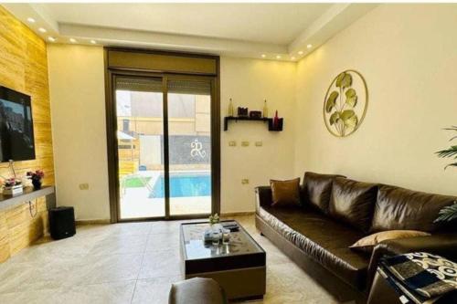 a living room with a leather couch and a table at Private Pool - Relax Chalet Deadsea in Amman