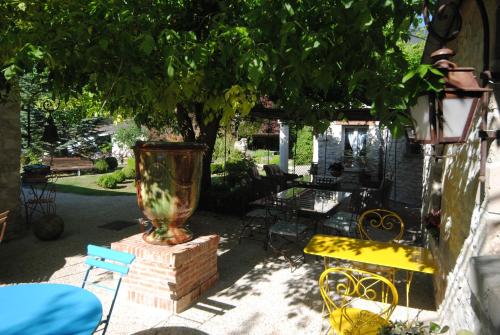 a patio with a vase and chairs under a tree at Les insolites du Grand Logis in Marchais