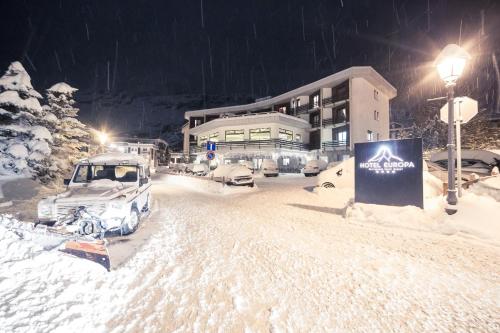 a parking lot covered in snow in front of a building at Hotel Europa in Breuil-Cervinia