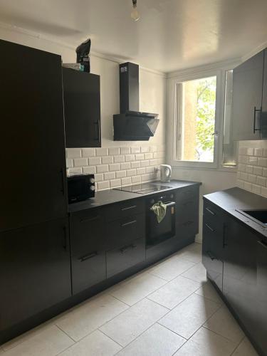 une cuisine avec des armoires noires et une fenêtre dans l'établissement Agréable Chambre Confortable, à Asnières-sur-Seine