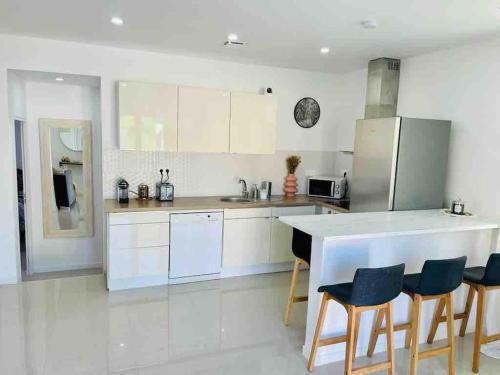 une cuisine avec des placards blancs et un comptoir avec des chaises dans l'établissement Magnifique MAISON de 80m2, proche CDG & PARIS, à Bonneuil-en-France