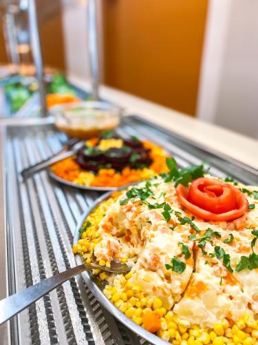 a buffet with a plate of food with corn and tomatoes at Hotel Zata - Econômico in Criciúma