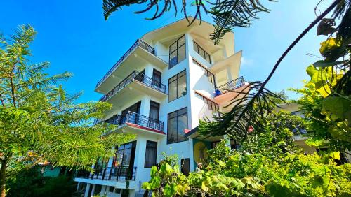a tall white building with balconies and trees at Hana Resort Landing Site in Bīr