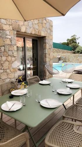 une table verte avec des assiettes et des chaises sur la terrasse dans l'établissement Location de charme l île rousse, à LʼÎle-Rousse