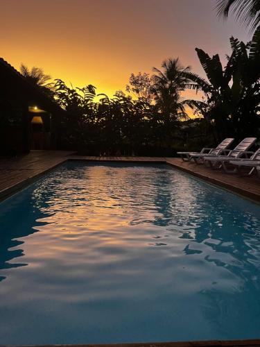 a swimming pool with chairs and a sunset in the background at Moana Ilhabela in Ilhabela