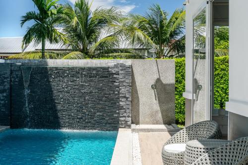 a swimming pool with two chairs next to a brick wall at Friendly Kamala Garden View in Kamala Beach