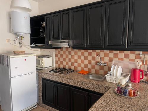 eine Küche mit schwarzen Schränken und einem weißen Kühlschrank in der Unterkunft Tamraght apartment with Pool access in Tamraght Ouzdar