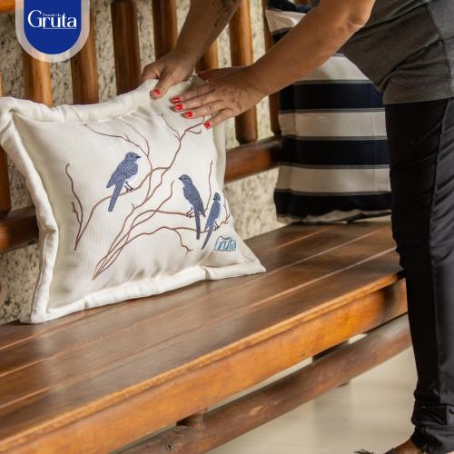 una donna in piedi su una panchina che tiene in mano un cuscino con degli uccelli sopra di Hotel Pousada da Gruta a Caratinga