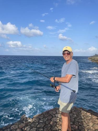 a man standing on a rock holding a fishing rod at Real Jamaica - 5 Cabins right beside the sea in Oracabessa