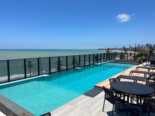 a swimming pool with tables and chairs and the ocean at Beach Haus beira mar bessa in Tambaú
