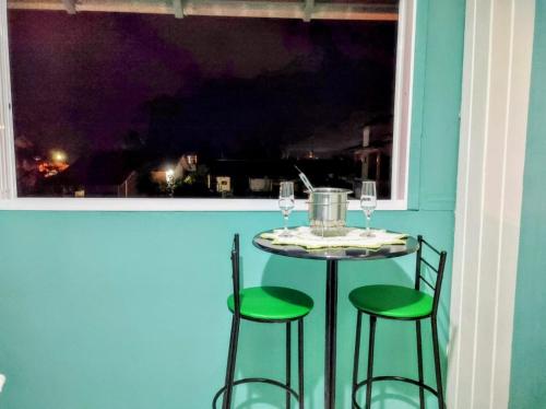 una mesa con 2 sillas verdes y una ventana en Apto com churrasqueira 500m do mar com vista da salaSacada para horizonte, en São Francisco do Sul