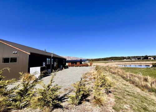 a building with a gravel road next to a body of water at Hazel's House - Lake Tekapo in Lake Tekapo