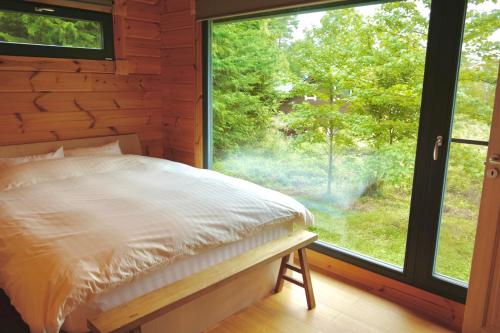 a bedroom with a bed and a large window at パインズコテージ八ヶ岳 トゥースラ in Hokuto
