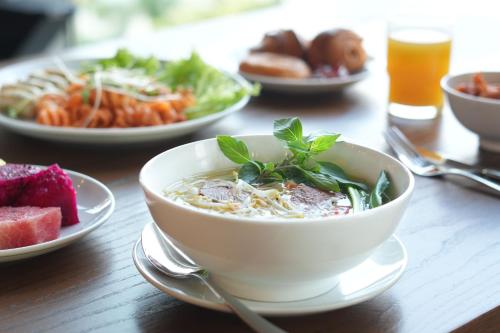 a bowl of soup on a table with plates of food at Wink Icon Hotel Danang Riverside - 24hrs Stay & Rooftop Pool Bar in Da Nang