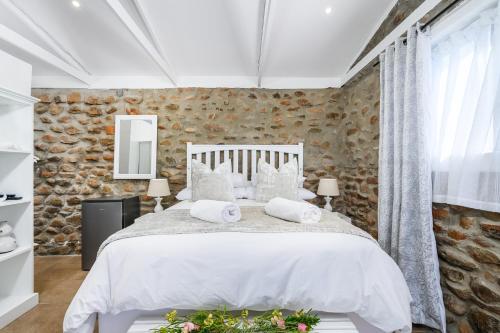 una camera da letto con un letto bianco e un muro di pietra di Le Petit Karoo a Oudtshoorn