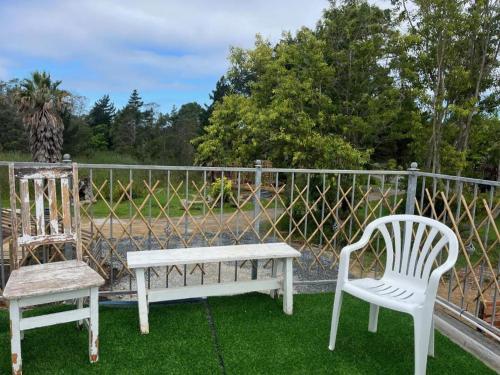 two white chairs and a bench on a yard at Forest Gate Brewery & Distillery Backpackers in Plettenberg Bay