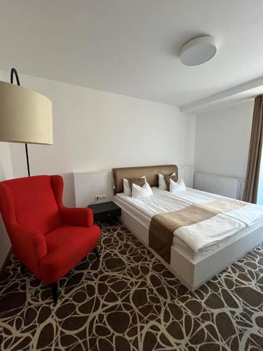 a bedroom with a bed and a red chair at Bassiana Hotel és Étterem in Sárvár
