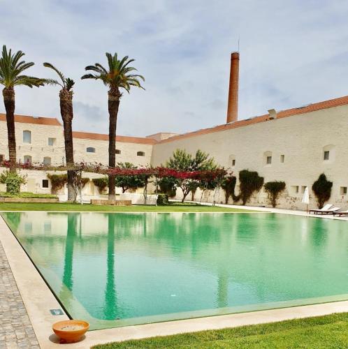 a swimming pool in front of a building with palm trees at Apartamento Convento das Bernadas Tavira in Tavira