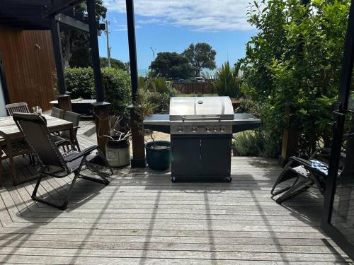 a grill on a patio with a table and chairs at Ahipara Beach Front, modern stylish bach in Ahipara