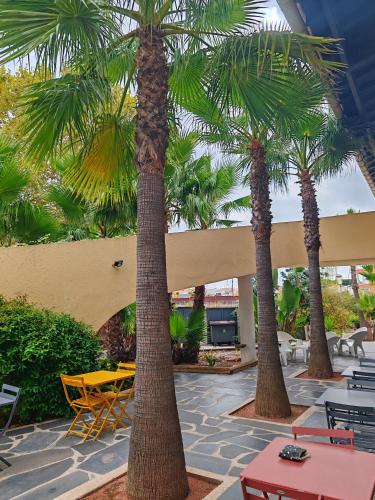 a patio with palm trees and a yellow table and chairs at Résidence Agathéa - Centre Port - Cap d'Agde in Cap d'Agde