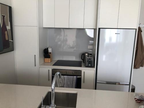 a kitchen with white cabinets and a sink and a refrigerator at Central Auckland condo, 2Br, 2Brm, pool, gym, study in Auckland