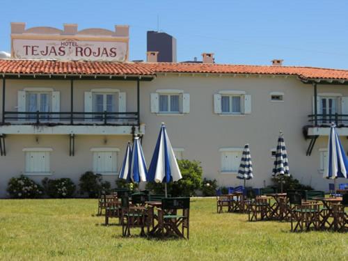 un edificio con tavoli e ombrelloni di fronte a un edificio di Hotel Tejas Rojas a Villa Gesell