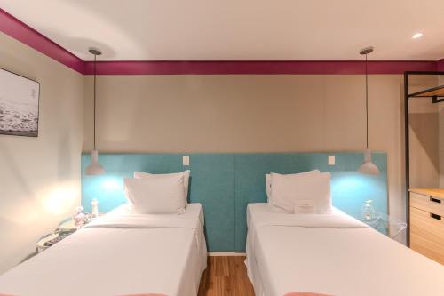 two beds in a room with white sheets and a green wall at Hotel Heritage in Sao Paulo