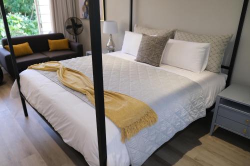 a bedroom with a white bed with a yellow blanket on it at High Hedges Guest Suites Constantia in Cape Town