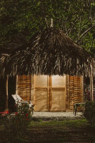 a hut with a chair and a straw umbrella at Magic Green Dentro del Parque Tayrona in El Zaino