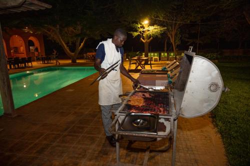 a man cooking food on a grill next to a pool at Lodge du Ranch de Bandia in Sindia