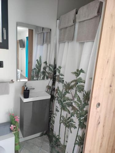 La salle de bains est pourvue d'un lavabo et de palmiers sur le rideau de douche. dans l'établissement Logement proche Caen et plages, à Colombelles