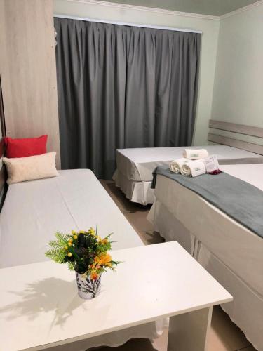 a room with two beds and a table with a vase of flowers at Hotel e Pousada Caroline in Foz do Iguaçu