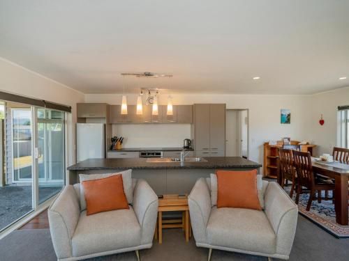 a living room with two chairs and a kitchen at Unwind on The Fairway - Matarangi Holiday Home in Whitianga