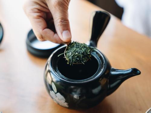 a person holding a black tea pot with grass on it at RITA Yame Fukushima in Yame