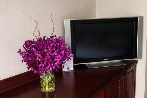a vase of purple flowers on a table next to a tv at City Lodge Bangkok in Bangkok