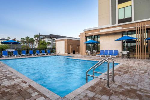 a large swimming pool with blue chairs and umbrellas at Hilton Garden Inn Orlando I-4 Millenia Blvd Mall in Orlando