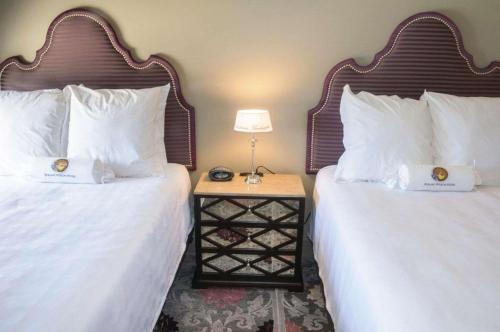two beds with white pillows and a night stand with a lamp at The Bolling Wilson Hotel in Wytheville