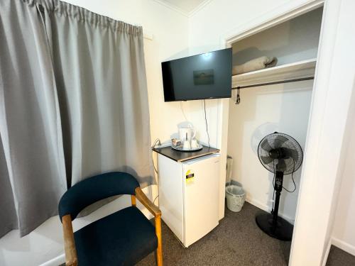a room with a tv and a chair and a fan at Rainbow Motel & Guest House in Tauranga