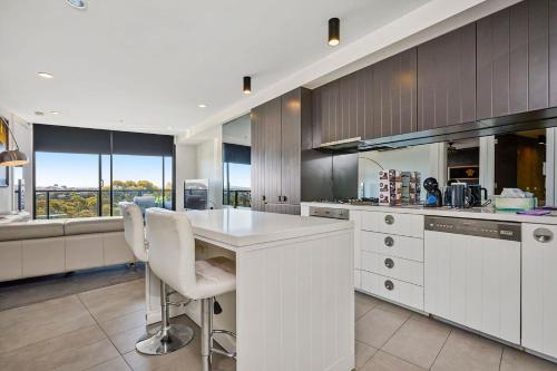 a kitchen with white cabinets and a counter with chairs at Riviera Edgewater Maribyrnong in Melbourne