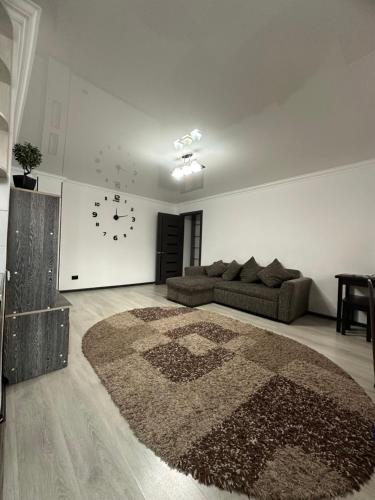 ein Wohnzimmer mit einer Couch und einer Uhr an der Wand in der Unterkunft Апартамент in Qaraghandy