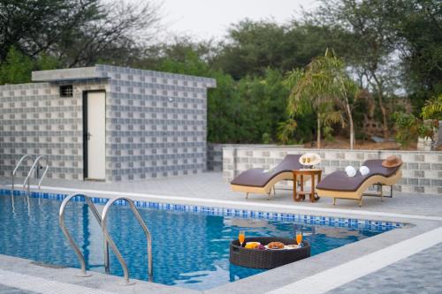 a pool with two chairs and a table next to it at ELIVAAS 5 BHK With Pvt Pool & Garden - Zenora in Gurgaon